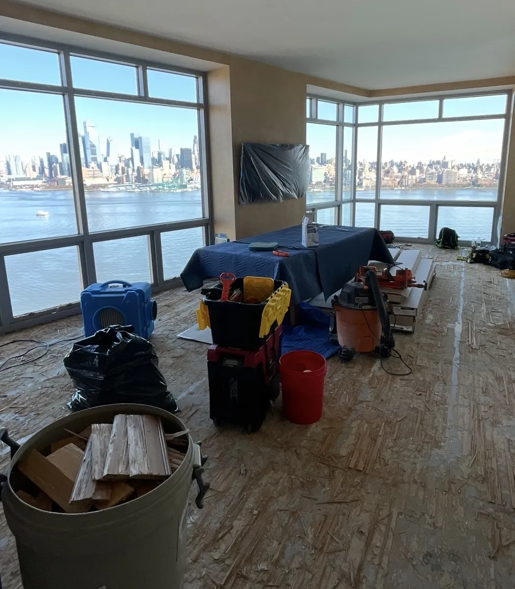 Condo living room with flooring removed to the subfloor, tools and equipment on site, Manhattan skyline through the windows