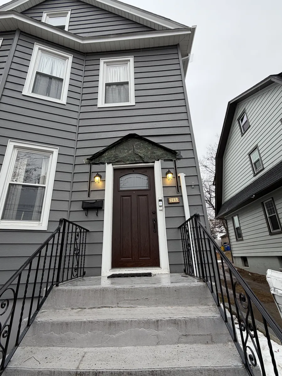 Front entry of a gray-sided house with a small decorative pediment over the door